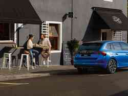 Blauer SKODA steht neben einem kleinen Kaffeehaus, wo Mann und Frau sitzen