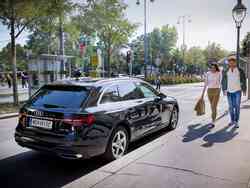 Frau und Mann gehen an der Beifahrer-Tür eines schwarzen Audi Kombis vorbei