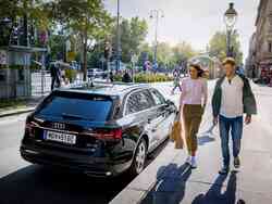 Frau und Mann gehen an der Beifahrer-Tür eines schwarzen Audi Kombis vorbei