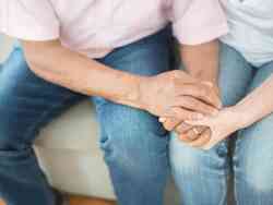 Zwei Personen sitzen nebeneinander und halten sich an den Händen.