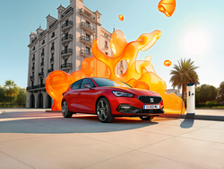 Seitliche Ansicht des SEAT Leon vor einem Gebäude. Im Hintergrund sind abstrakte, orange Farbblasen