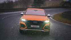 Ein oranger Audi RS Q8 von vorne. Die Scheinwerfer sind eingeschaltet.