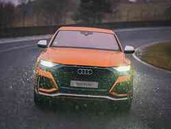 Ein oranger Audi RS Q8 von vorne. Die Scheinwerfer sind eingeschaltet.
