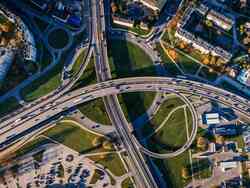 Ein Verkehrssystem aus Vogelperspektive fotografiert: Unter zwei kreuzenden Autobahnen befindet sich ein Kreisverkehr. Rundherum stehen Gebäude.