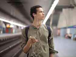 Ein Mann mit Kopfhörern und seinem Smartphone in der Hand steht an einer U-Bahn Station und schaut fragend nach rechts. Ein Mann mit Kopfhörern und seinem Smartphone in der Hand steht an einer U-Bahn Station und schaut fragend nach rechts.