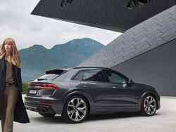 Eine Frau geht vor einem grauen Audi RS Q8.