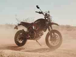 Eine Ducati steht in einer Wüste. Rundherum ist Sand aufgewirbelt.