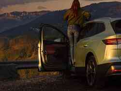 Eine Frau steht in der Fahrertür von einem geparkten Skoda Enyaq bei Sonnenuntergang.