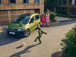 Junge spielt mit seinem Vater Fußball vor einem goldenen VW-Caddy
