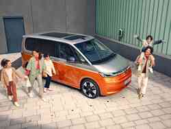 Familie mit mehreren Kindern steht neben einem silber-orangen VW-Multivan