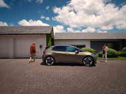 Bronzefarbener VW Elektro-Kompaktwagen steht vor zwei Personen vor einem Haus