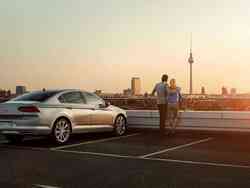 Ein Mann und eine Frau stehen umschlungen auf einem Parkplatz neben einem silbernen VW während die Sonne untergeht
