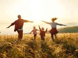 Eine Mann, eine Frau und zwei Kinder toben auf einem Feld im Sonnenuntergang herum