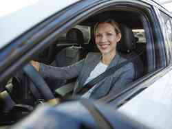 Frau sitzt am Steuer eines Autos und lacht durch das geöffnete Fenster