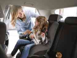 Frau schnallt ein kleines Mädchen im Kindersitz eines Autos auf der Rückbank an