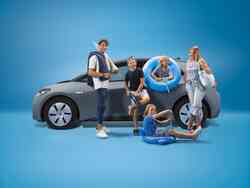 Eine Familie steht mit Schwimmzubehör bepackt vor einem grauen VW.