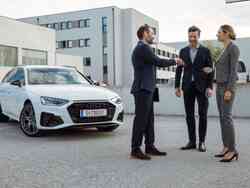 Drei Personen in formeller Kleidung unterhalten sich vor einem weißen Audi