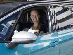 Frau sitzt am Steuer eines Autos und lacht aus dem geöffneten Autofenster