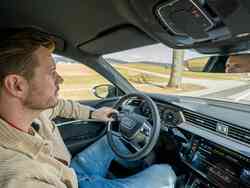 Ein Mann sitzt auf dem Fahrersitz eines Audis und hält das Lenkrad mit einer Hand während er aus der Windschutzscheibe schaut.