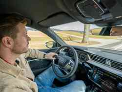 Ein Mann sitzt auf dem Fahrersitz eines Audis und hält das Lenkrad mit einer Hand während er aus der Windschutzscheibe schaut. Ein Mann sitzt auf dem Fahrersitz eines Audis und hält das Lenkrad mit einer Hand während er aus der Windschutzscheibe schaut.