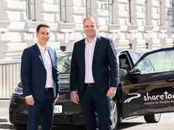 Zwei Männer (Steffen Gersch, Geschäftsführer Porsche Mobility, und Dominik Grimm, Head of Business Development sharetoo/Porsche Mobility)  in Anzug stehen vor einem sharetoo VW und schauen in die Kamera.