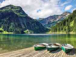 der Vilsalpsee in Tirol: Auf einem Steg sind drei Boote zu sehen. Hinter dem See sieht man grün bewachsene Berge.