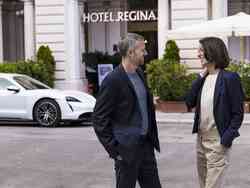 Mann und Frau in Business-Kleidung stehen vor einem weißen Porsche vor dem Hotel Regina in Wien