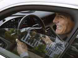 Mann sitzt am Steuer eines Autos und lacht durch das halb geöffnete Fahrerfenster