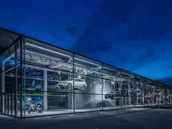 Ein Gebäude der Porsche Holding ist zu sehen. Durch die Glaswand kann man verschiedene Autos dekorativ aufgestellt erkennen.