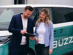 Ein Mann und eine Frau stehen vor einem VW ID Buzz und schauen auf ein Tablet