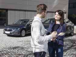 Ein Mann und eine Frau reden miteinander. Hinter ihnen parkt ein grauer Skoda und ein anderes Auto.