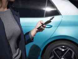 Eine Frau hält ihr Smartphone in der Hand. Hinter ihr steht ein blaues Fahrzeug.