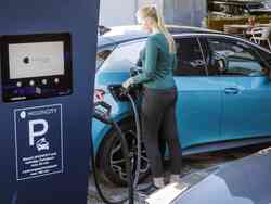 Eine Frau steckt ihr blaues Fahrzeug an einer Elektrotankstelle an.