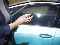 Eine Frau steht neben einem blauen Auto und schaut auf ihr Smartphone.