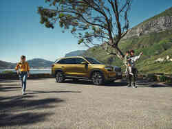 Geparkter Škoda Kodiaq. Links und rechts vom Auto stehen eine Frau und ein Mann, der ein Kind hält